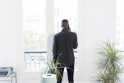 Rückenansicht eines Geschäftsmannes, der im Büro telefoniert und aus dem Fenster schaut - GRSF00031