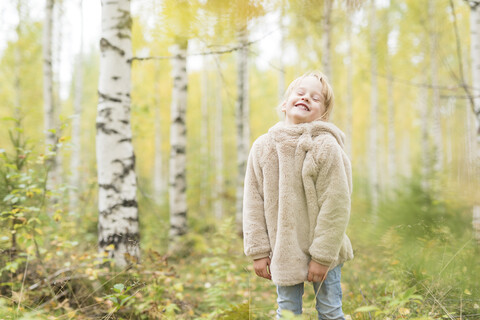 Porträt eines lachenden blonden Mädchens, das im herbstlichen Wald spielt, lizenzfreies Stockfoto