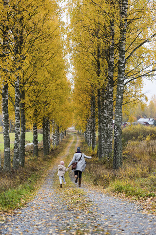 Finland, Kuopio, back view of mother and little daughter running side by side in autumn stock photo