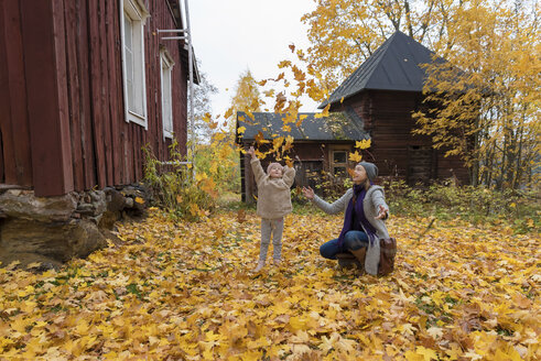 Finnland, Kuopio, Mutter und kleine Tochter, die Herbstblätter in die Luft werfen - PSIF00189