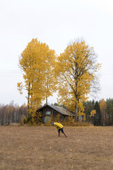 Finnland, Kuopio, Frau in gelber Regenjacke sammelt Herbstblätter - PSIF00196