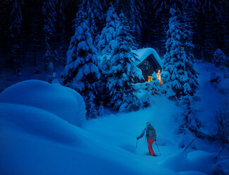 Österreich, Bundesland Salzburg, Schneeschuhwandern, Frau bei Hütte in der Nacht - HHF05570