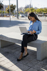 Businesswoman using laptop, holding smartphone - MAUF01829