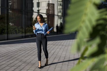 Businesswoman using smartphone, laptop bag - MAUF01847