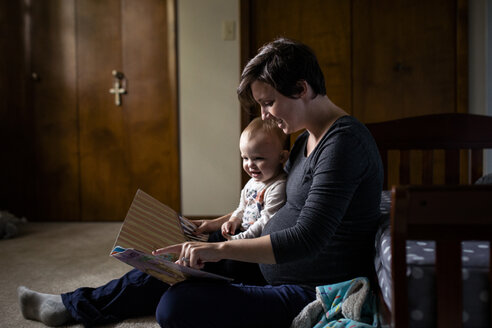 Schwangere Frau zeigt ihrer Tochter ein Bilderbuch, während sie zu Hause sitzt - CAVF58424