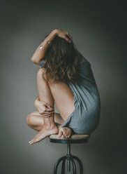 Depressive Frau in voller Länge mit verdunkeltem Gesicht auf einem Hocker an der Wand sitzend - CAVF58427