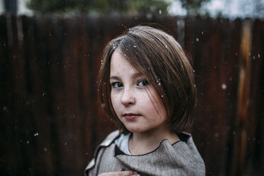 Porträt eines selbstbewussten Mädchens im Hinterhof bei Schneefall - CAVF58453
