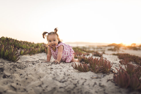 Porträt eines kleinen Mädchens, das am Strand im Sand krabbelt, bei klarem Himmel - CAVF58461