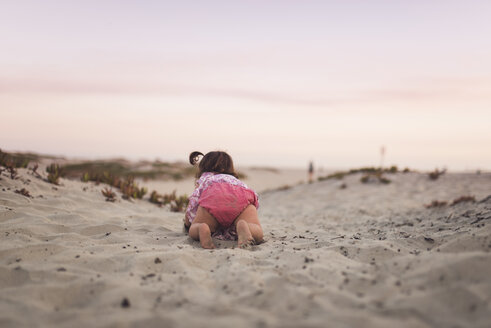 Rückansicht eines kleinen Mädchens, das am Strand gegen den Himmel bei Sonnenuntergang auf dem Sand krabbelt - CAVF58462