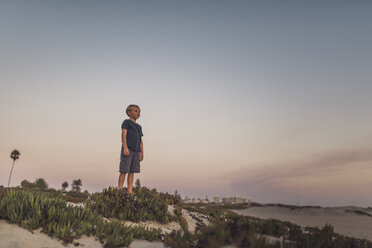 Full length of boy standing on sand at beach against sky during sunset - CAVF58463