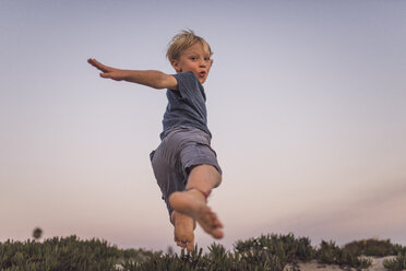 Low angle view of boy jumping on sand at beach against sky during sunset - CAVF58465
