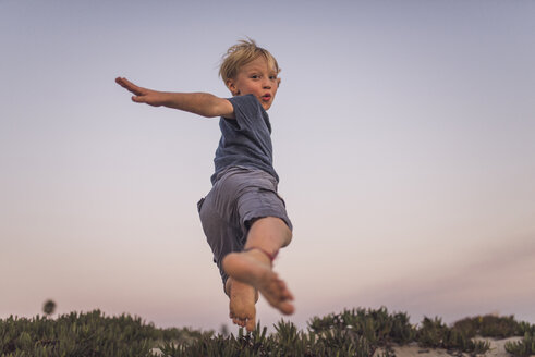 Niedriger Blickwinkel des Jungen springen auf Sand am Strand gegen den Himmel bei Sonnenuntergang - CAVF58465