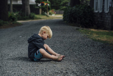 Seitenansicht eines Jungen, der mit Steinen spielt, während er auf der Straße sitzt - CAVF58472