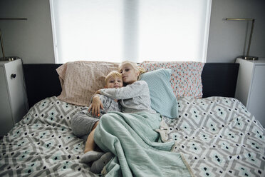 High angle portrait of sister embracing brother while lying on bed at home - CAVF58473