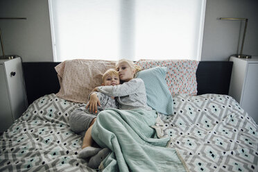 Hochformatiges Porträt einer Schwester, die ihren Bruder umarmt, während sie zu Hause auf dem Bett liegt - CAVF58473