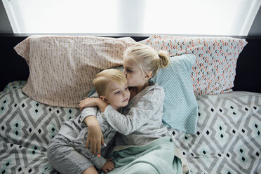 High angle view of sister kissing brother while lying on bed at home - CAVF58474