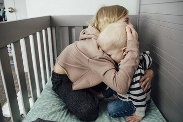 Girl embracing brother while sitting in crib - CAVF58481