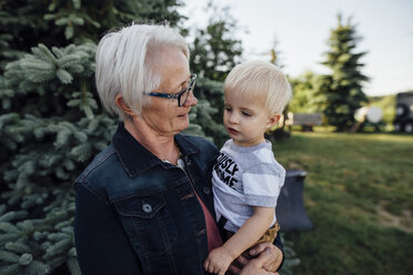 Grandmother carrying grandson while standing at farm - CAVF58486