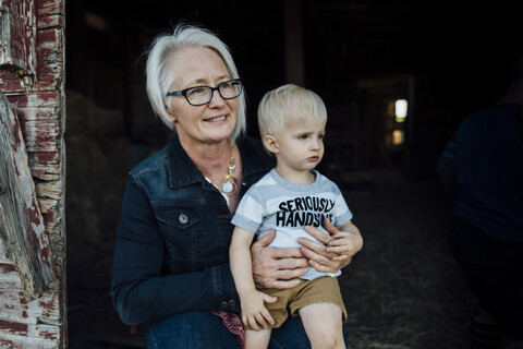 Großmutter mit Enkel an der Scheune sitzend, lizenzfreies Stockfoto