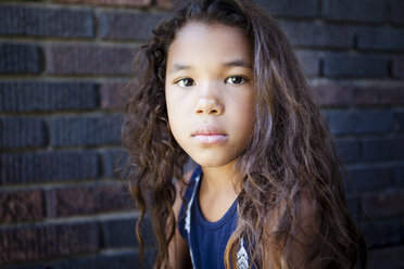 Portrait of girl with tousled hair against brick wall - CAVF58510