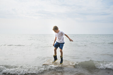 Junge springt in voller Länge auf Felsen im Meer gegen den Himmel - CAVF58554