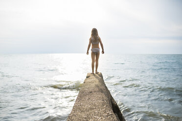 Rear view of girl standing on jetty at beach against sky - CAVF58556