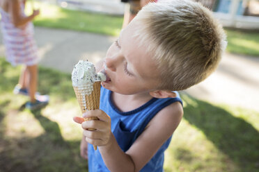 Boy licking melting ice cream while standing at backyard - CAVF58557
