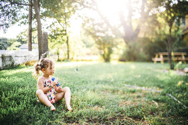 Full length of girl with popsicle sitting on grassy field at backyard - CAVF58560