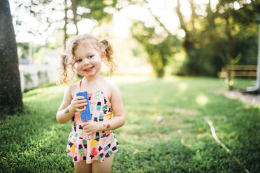 Smiling girl with popsicle standing on grassy field at backyard - CAVF58561