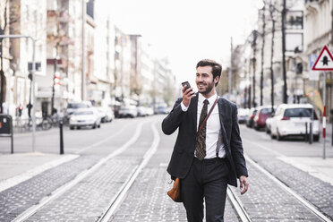 Businessman talking on mobile phone walking by railroad tracks in city - CAVF58567