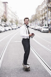 Businessman using phone while skateboarding on road in city - CAVF58569