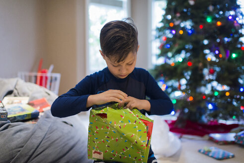 Junge packt Weihnachtsgeschenk ein, während er zu Hause sitzt - CAVF58606