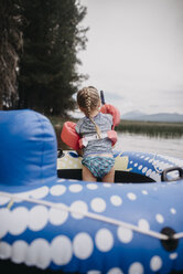 Rückansicht eines Mädchens mit Schwimmflügeln auf einem Schlauchboot auf einem See - CAVF58612