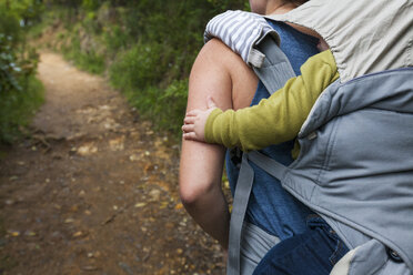 Rückansicht einer Mutter, die ihren Sohn im Kinderwagen trägt, während sie im Wald spazieren geht - CAVF58650