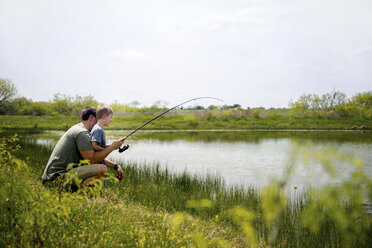 Seitenansicht von Vater und Sohn beim Fischen im Teich gegen den Himmel - CAVF58654