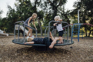 Geschwister spielen auf einem Karussell auf dem Spielplatz - CAVF58672