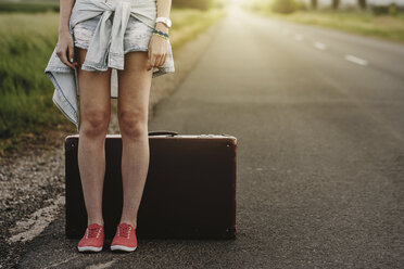 Low section of woman standing by suitcase on road - CAVF58767