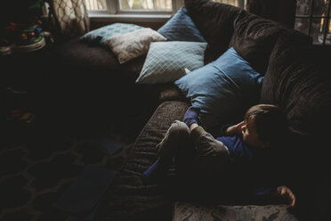 High angle view of thoughtful boy looking away while relaxing on sofa at home - CAVF58769