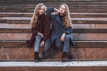 Portrait of sisters sitting on steps in city during winter - CAVF58770