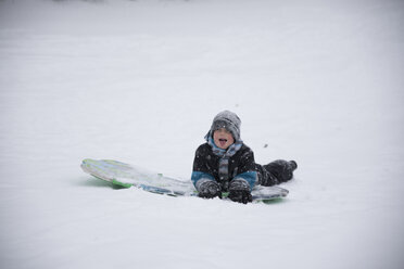 Unbekümmerter Junge mit Schlitten auf verschneitem Feld bei Schneefall - CAVF58777