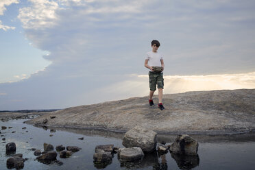 Boy carrying rocks while walking on Arabia Mountain against cloudy sky - CAVF58789