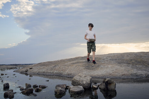 Boy carrying rocks while walking on Arabia Mountain against cloudy sky - CAVF58789