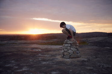 Junge sitzt auf Felsen am Arabia Mountain gegen bewölkten Himmel bei Sonnenuntergang - CAVF58794