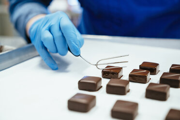 Mittelteil eines Kochs, der mit einer Gabel in ein Tablett getauchte Schokolade hält - CAVF58803
