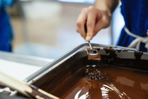 Abgeschnittene Hand einer Köchin, die Schokolade in einer Fabrik in Fondue taucht, lizenzfreies Stockfoto