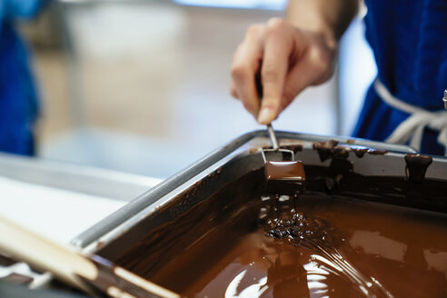 Abgeschnittene Hand einer Köchin, die Schokolade in einer Fabrik in Fondue taucht - CAVF58804