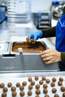 Mittelteil einer Köchin, die in einer Fabrik Schokoladenstücke in Fondue taucht - CAVF58809