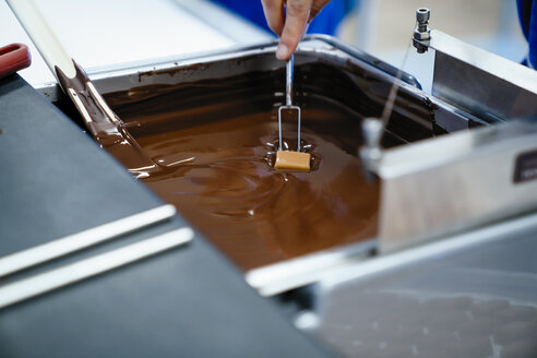 Abgeschnittene Hand einer Köchin, die Schokolade mit einer Gabel in Fondue eintaucht, in einer Fabrik - CAVF58810