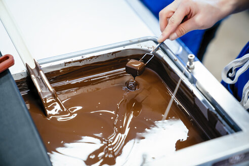 Abgeschnittene Hand einer Köchin, die Schokolade mit einer Gabel in Fondue eintaucht - CAVF58811