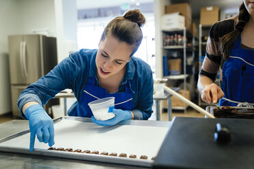 Mittelteil eines weiblichen Kochs, der neben einem Mitarbeiter steht, der Schokoladenstücke in einem Tablett in einer Fabrik garniert - CAVF58813